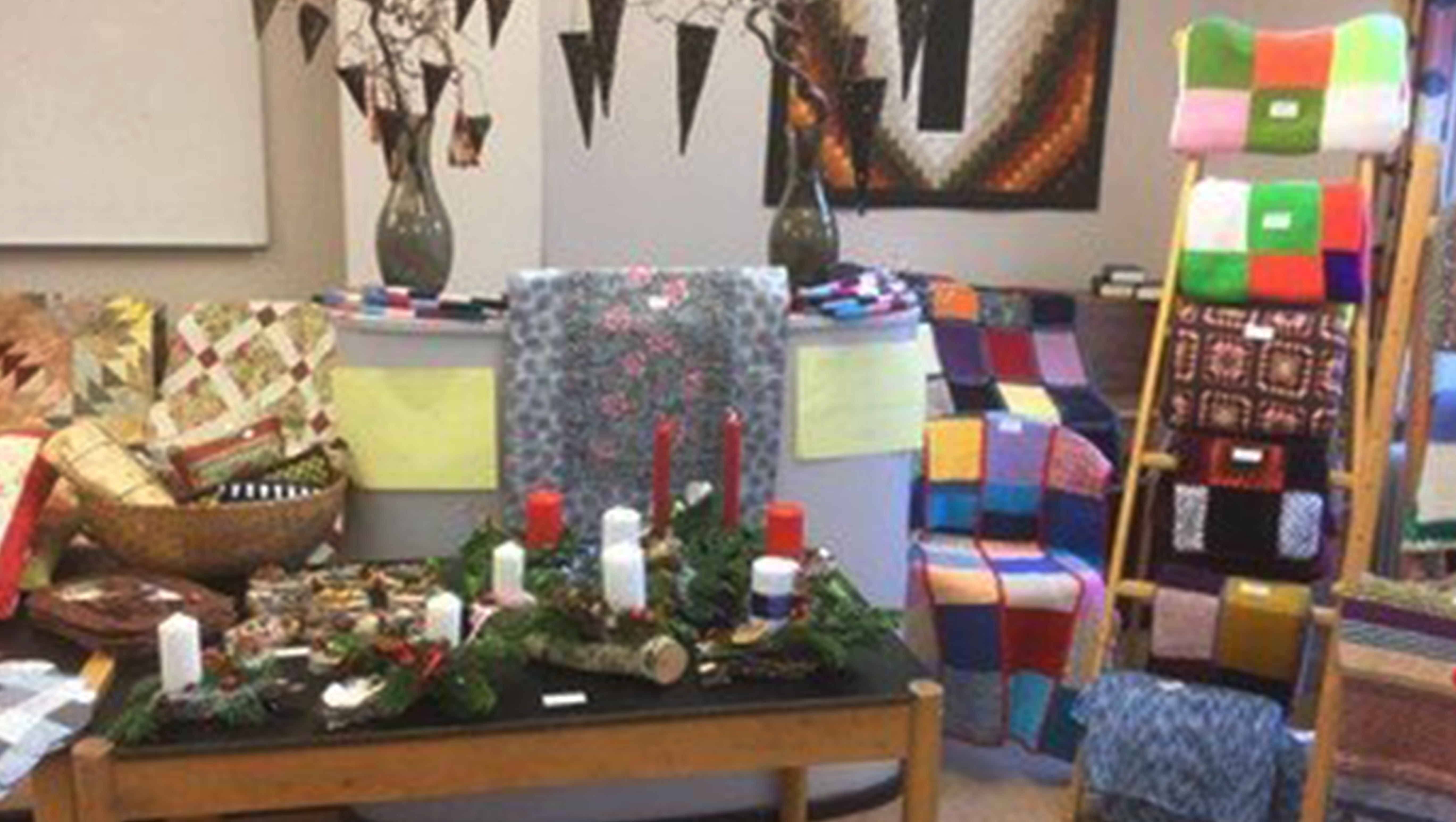 Et bord med adventskranse, stearinlys og strikkede tæpper i baggrunden.