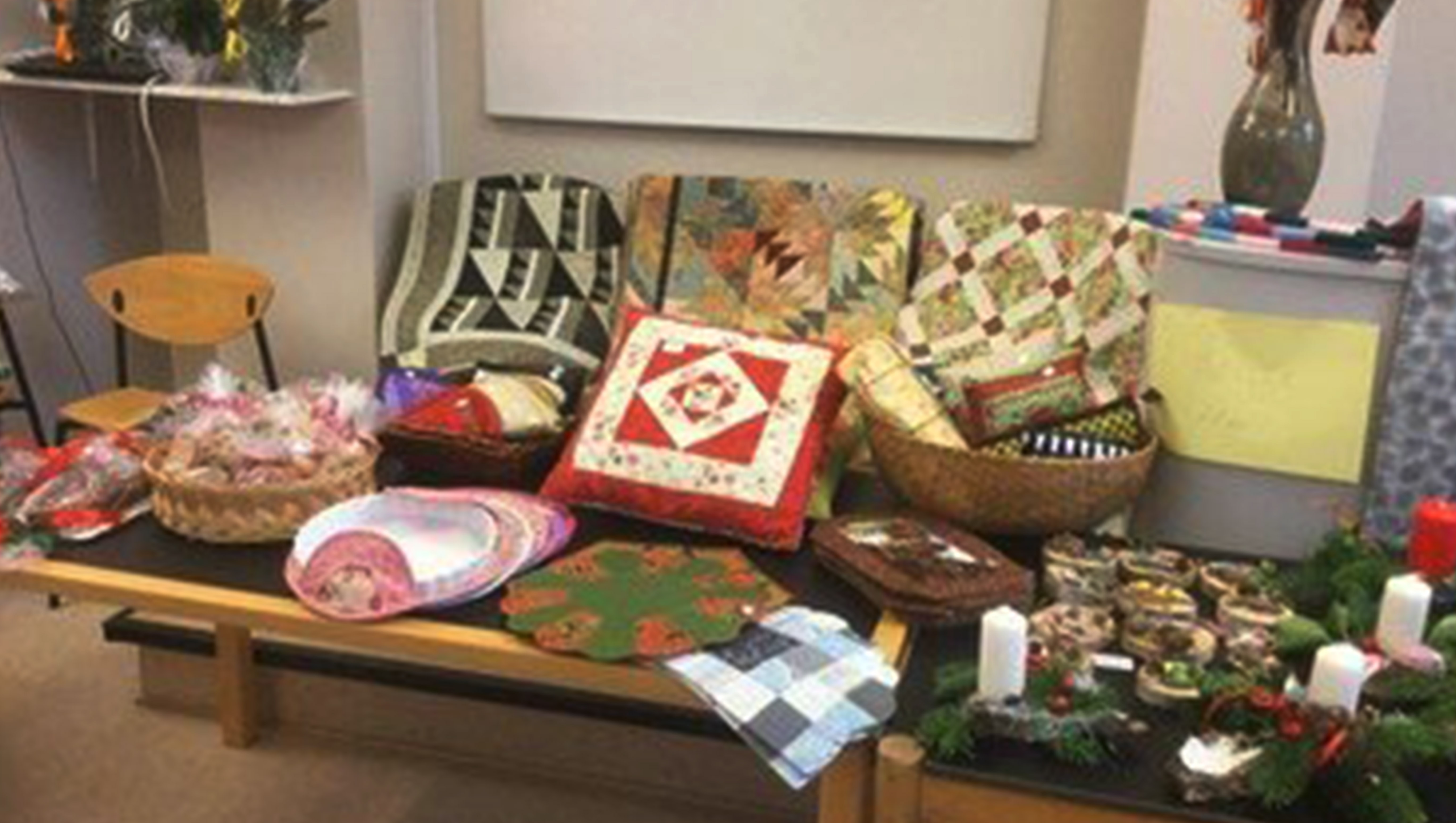Udstilling af hjemmelavede patchwork-puder og juledekorationer på et bord.