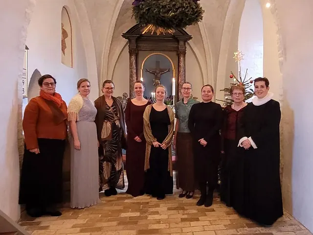 En gruppe kvinder og en præst står samlet foran alteret i en lys kirke.