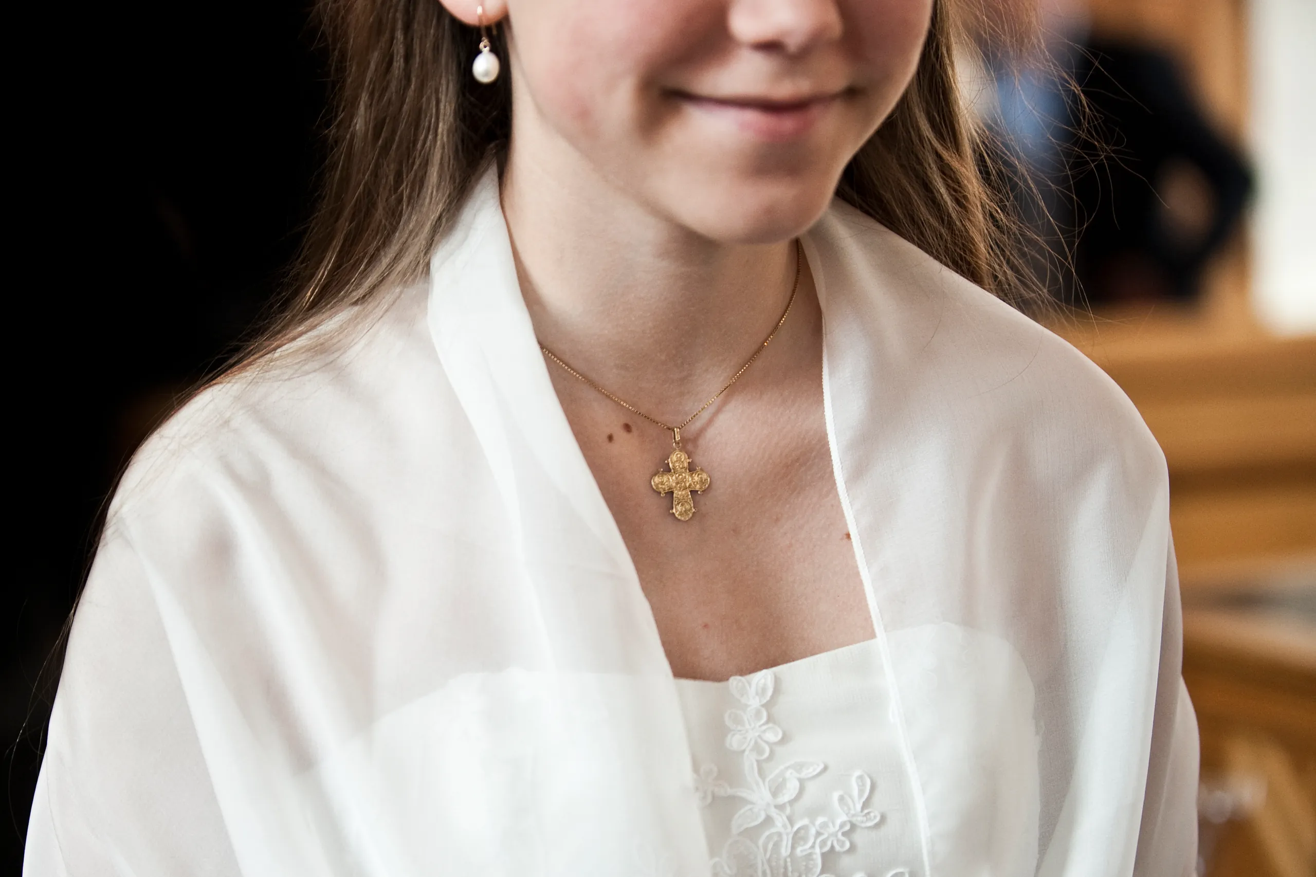 Nærbillede af en pige i hvid kjole med et guldkors om halsen.