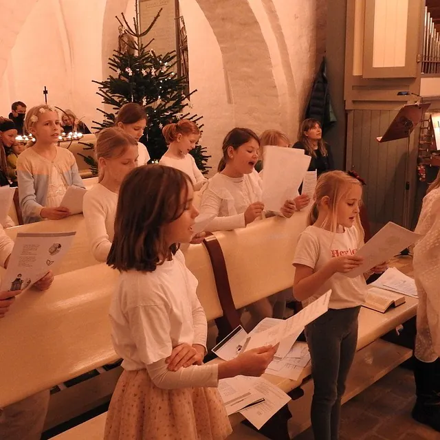 Et børnekor der synger fra sangark i en kirke ved juletid.
