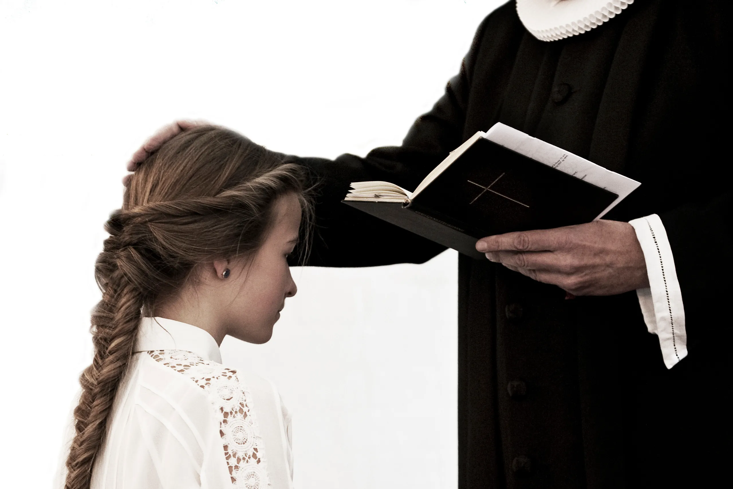 En præst med en bibel lægger hånden på hovedet af en konfirmand.