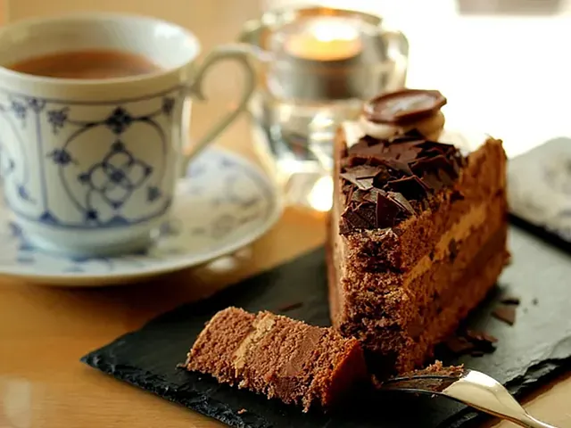 Et stykke chokoladekage på en skiferplade ved siden af en kop kaffe og et tændt stearinlys.
